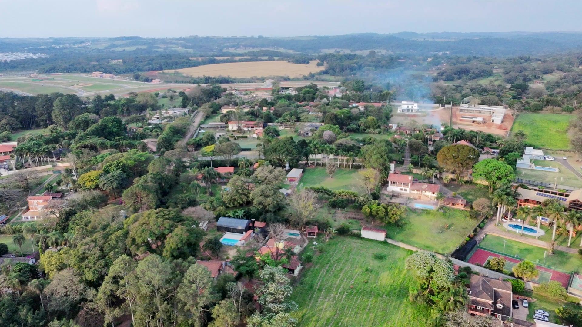 Vista aérea de uma região de chácaras com casas, gramados e árvores, e morros ao fundo