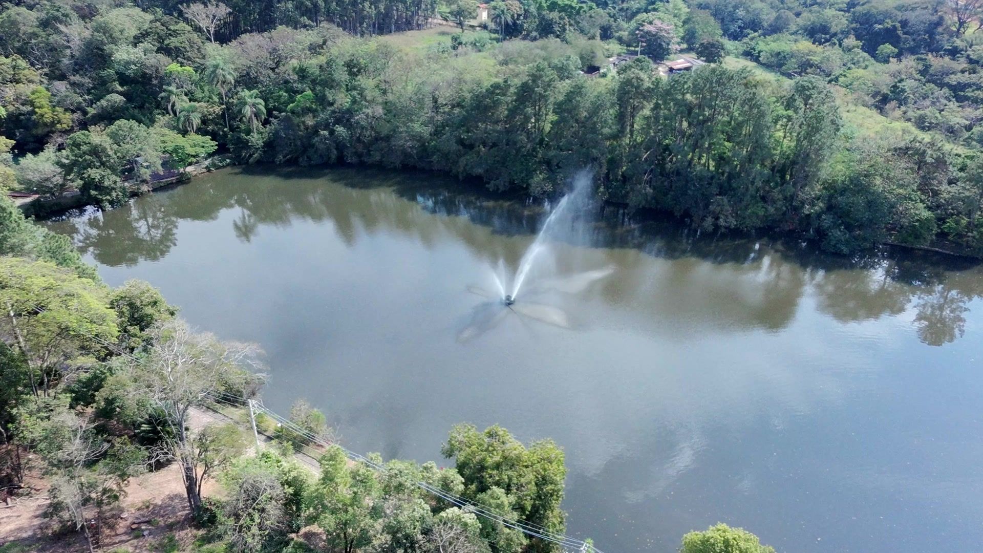 Vista aérea de um lago com um chafariz no centro, cercado de árvores