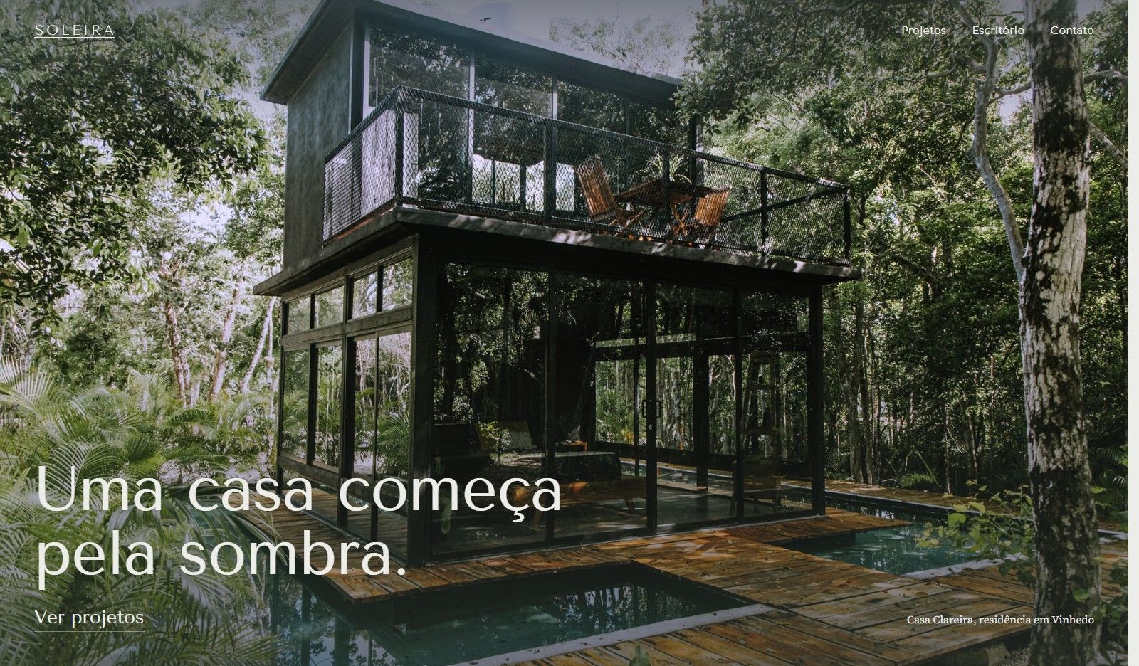 Primeira tela do site Soleira, com uma casa de vidro entre árvores e o título Uma casa começa pela sombra